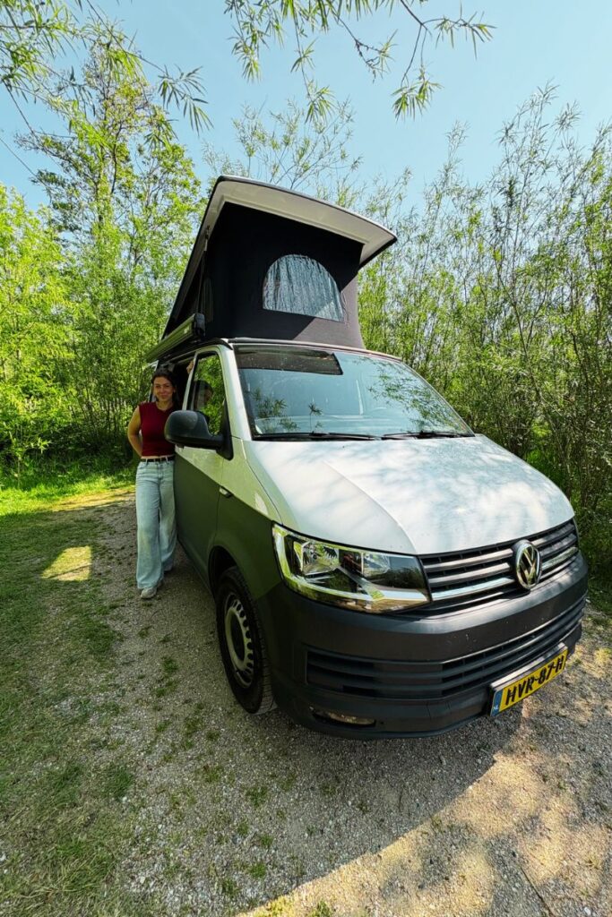 Michelle bij de ingang van haar camper, omringd door groen en natuur